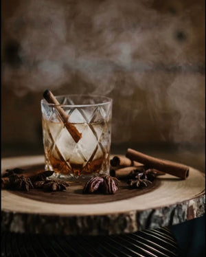 Smoky Pecan Old Fashioned cocktail with cinnamon sticks on a rustic wood slice platter
