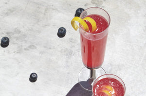 Blueberry French 75 cocktail in a champagne flute with a lemon peel twist garnish