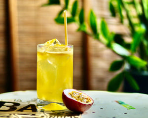 Passionfruit Staycation cocktail in a highball glass next to half a fresh passionfruit