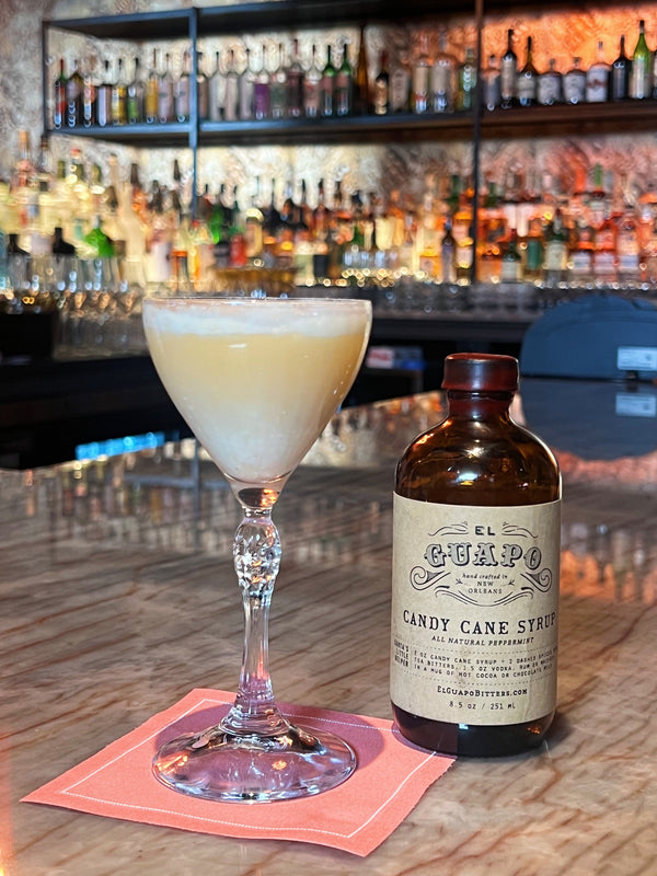 The Jolie Stinger cocktail next to a bottle of El Guapo Candy Cane Syrup.
