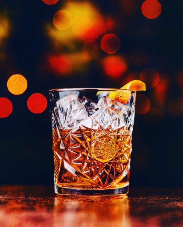 Tequila Old Fashioned cocktail with an orange peel garnish against a bokeh background