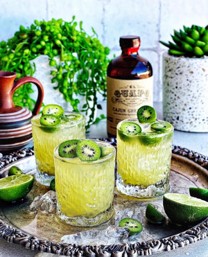Irish Gin Jig cocktails with kiwi slices on a tray next to El Guapo Cajun Grenadine