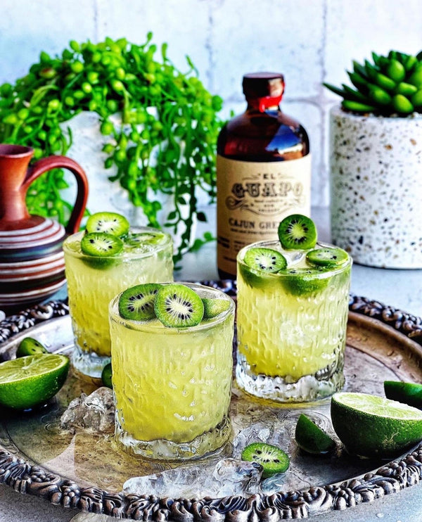 Irish Gin Jig cocktails with kiwi slices on a tray next to El Guapo Cajun Grenadine