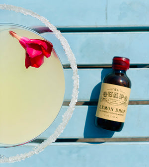 Sugar-rimmed Lemon Drop martini cocktail with El Guapo mixer bottle on blue wood