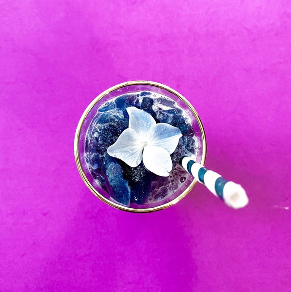 Blue Butterfly Pea Flower drink with a floral garnish on a bright purple background