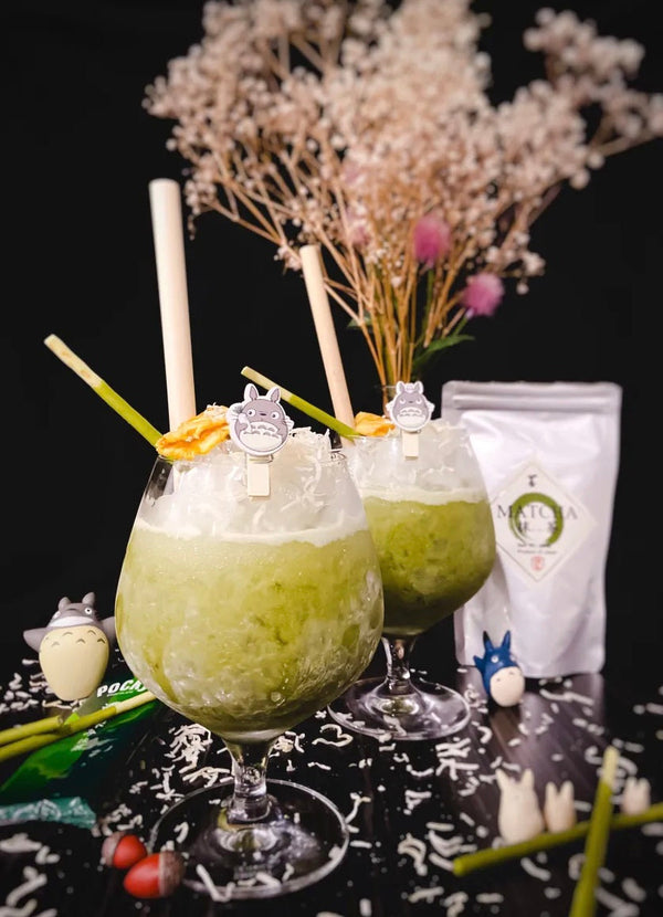 Two green Totoro's Dream matcha rum cocktails with coconut flakes and tiny Totoro figures