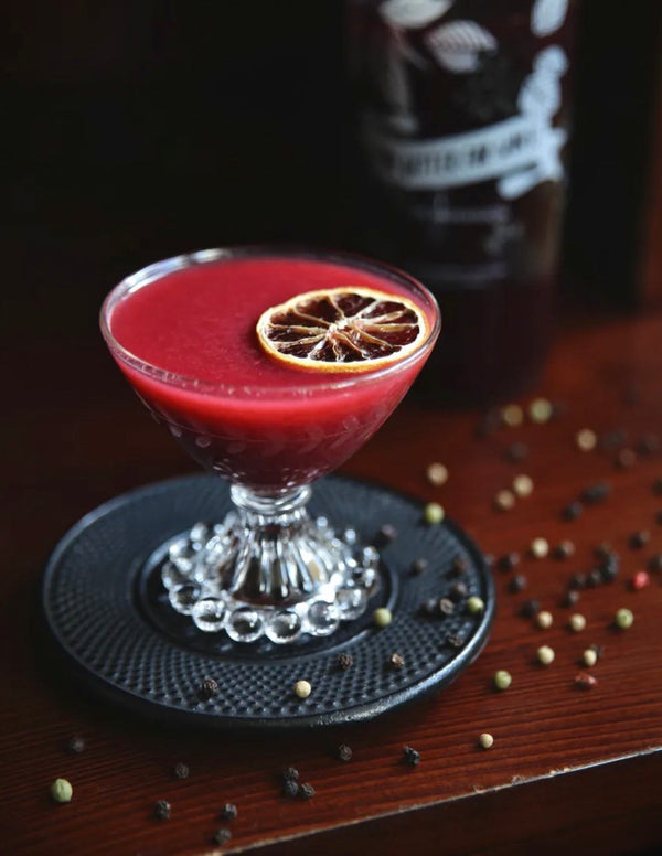 A vibrant red Two Twists cocktail topped with a dehydrated lime wheel in a crystal coupe