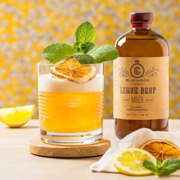 Whiskey Sour garnished with mint next to a bottle of El Guapo Lemon Drop Mixer