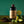 Bottle of El Guapo Black Lime Margarita Mixer styled with fresh limes and black lime powder on a wooden surface with a green background