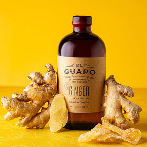 16.5 oz lottle of El Guapo Ginger Syrup with ginger roots on a yellow background