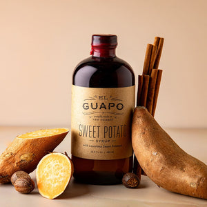 Bottle of Guapo Sweet Potato Syrup with sweet potatoes and cinnamon sticks on a beige background