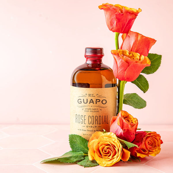 Bottle of 16.5 oz El Guapo Rose Cordial with roses on a pink background