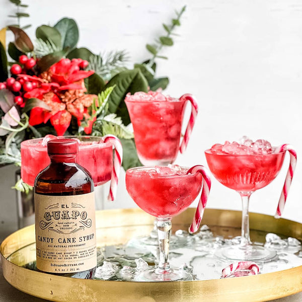 Red cocktails with candy canes and a bottle of El Camino Candy Cane Syrup on a gold tray.