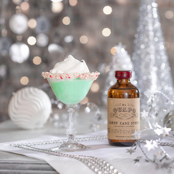 Mint green grasshopper cocktail with whipped cream and candy cane rim next to a bottle of candy cane syrup on a festive background.