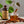 Small bottle of El Guapo sweet potato syrup with an old fashioned garnished with a cinnamon stick surrounded by whole pecans on a wooden surface.