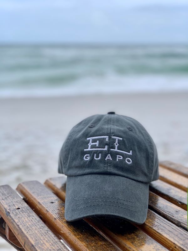El Guapo embroidered logo baseball cap on a wooden bench at the beach.